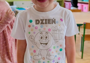 Chłopiec pozuje do zdjęcia. Na sobie ma koszulkę z napisem "Dzień Kropki".