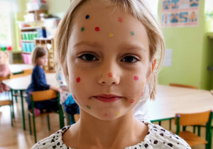 Dziewczynka pozuje do zdjęcia. Na twarzy ma namalowane kropki.