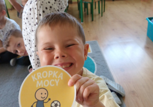 Chłopiec pozuje do zdjęcia i prezentuje koło z napisem "Kropka mocy".