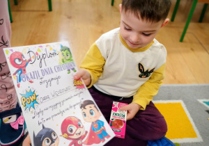 Nauczycielka wręcza chłopcu dyplom z okazji Dnia Chłopaka.