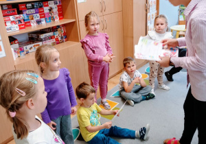 Nauczycielka wręcza chłopcu dyplom z okazji Dnia Chłopaka. W tle znajdują się pozostałe dzieci.