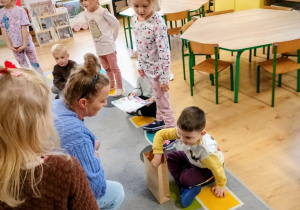 Chłopiec wyjmuje z torebki prezent. W tle znajdują się pozostałe dzieci.