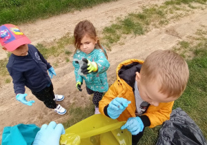 troje dzieci wrzuca znalezione śmieci do kolorowych worków do segregacji odpadów