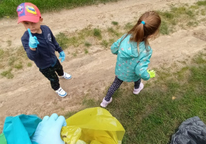 dwoje dzieci wrzuca znalezione śmieci do kolorowych worków do segregacji odpadów
