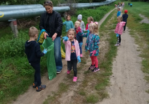 grupa dziec i pani trzymająca worek na dpady . sprzątają tereny obok "rur"