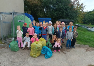 grupa dzieci pozuje do wspołnego zdjęćia po akcji sprzątania, obok stoją worki z odpadami, jakie dzieci zebrały