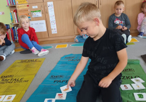 grupa dzieci w klasie bierze udziałw zajęciach edukacyjnych , na podłodze leżą kolorowe worki na odpady, chłopiec przyporządkowuje obrazki z odpadami do odpowiednich worków