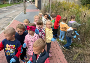 grupa dzieci , jedne stoją na chodniku, inne na łące, zbierają śmieci
