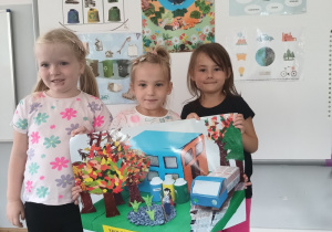 trzy dziewczynki w klasie, trzymają planszę edukacyjną pt. Ekologiczna szkoła