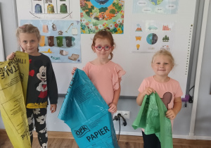 troje dziecie w klasie, trzymająkolorowe worki do segregacji odpadów