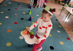 dziewczynka z tacąz jabłkami bierze udział w zabawie ruchowej, na drugim planie pozostałe dzieci