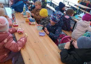 Dzieci siedzą przy stołach i jedzą zabrane ze sobą przekąski