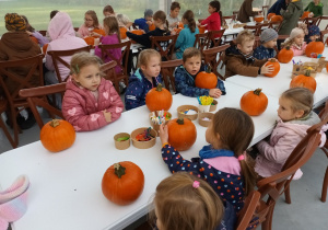 Dzieci siedzą przy stole i ozdabiają dynie.