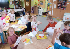 Dzieci siedzą przy stolikach i rozpakowują swoje pakiety do realizacji programu.