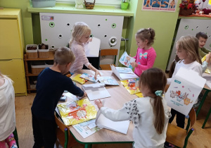 Dzieci siedzą przy stolikach i rozpakowują swoje pakiety do realizacji programu.