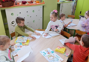 Dzieci siedzą przy stolikach i rozpakowują swoje pakiety do realizacji programu.