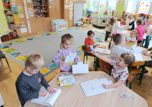 Dzieci siedzą przy stolikach i rozpakowują swoje pakiety do realizacji programu.