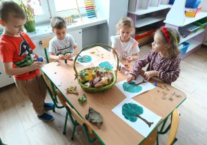 grupa dzieci przy stoliku wykonuje pracę plastyczną, na stole leży kosz z listkami