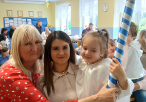 Pani Dyrektor, mama i dziewczynka pozują do wspólnego zdjęcia, dziewczynka trzyma ołówek do pasowania