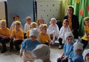kilkoro dzieci, w szatkach Duszków , siedzi na ławeczce podczas występu , obok nauczycielka i dzieci z innej grupy ze