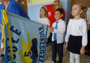 poczet sztandarowy - starszaki: dwie dziewczynki i chłopiec, który trzyma sztandarek przedszkola , na którym jest logo