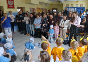 publiczność - rodzice biorą udział w zabawie ruchowej, naprzeciwko nich stoją dzieci
