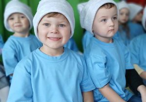 kilkoro dziec iprzebranyc hza smerfy siedzi na ławeczce podczas wystepów