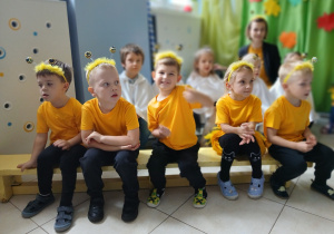 na pierwszym planie grupa dzieci przebranych za pszczółki - siedzą na ławeczce, z tyłu dzieci z grupy Duszki i nauczycielka