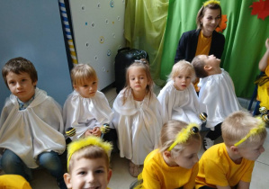 na pierwszym planie grupa dzieci przebranych za pszczółki - siedzą na ławeczce, z tyłu dzieci z grupy Duszki i nauczycielka