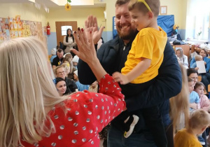 tata trzyma syna na rękach, mężczyzna przybija "piątkę" z panią dyrektor