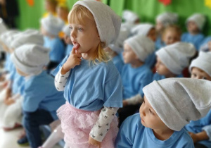 grupa dziec iprzebranyc hza smerfy siedzi na ławeczce podczas występu, jedna dziewczynka stoi