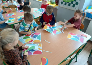 grupa dzieci pracuje przy stolikach, wycinają kolorowe elementy papierowych parasolek