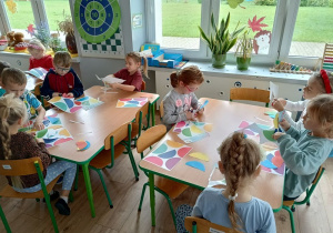 grupa dzieci pracuje przy stolikach, wycinają kolorowe elementy papierowych
