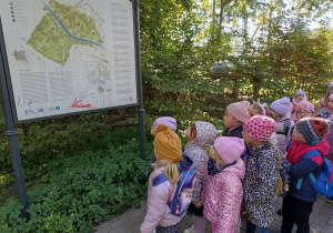grupa dzieci w parku miejskim, patrzą na umieszczoną tam tablicę z planem parku