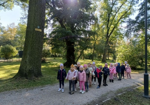 grupa dzieci w parku miejskim, stoją pod drzewem z tabliczką Samuel