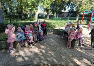 grupa dzieci w parku miejskim, siedzą na murku i posilają się