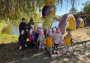 grupa dzeici z znauczycielkami pozuje do wspólnego zdjęcia przy wężu (instalacja), za nimi staw