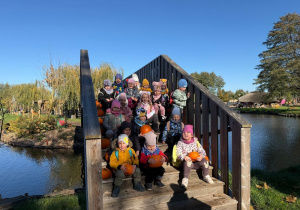 grupa dzieci siedzi na mostku, na drugim planie staw