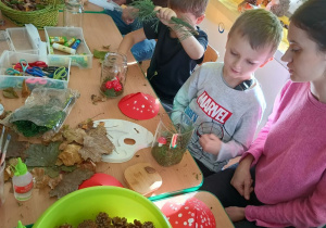 dzieci i rodzice tworzą a darów jesienie kompozycje w śłoikach. siedzą przy stołach z rozłożonymi matariałami do pracy