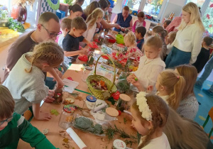 dzieci i rodzice tworzą a darów jesienie kompozycje w śłoikach. siedzą przy stołach z rozłożonymi matariałami do pracy