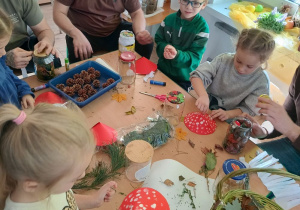dzieci i rodzice tworzą a darów jesienie kompozycje w śłoikach. siedzą przy stołach z rozłożonymi matariałami do pracy