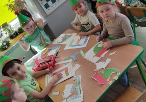 dzieci w czapkach elfów pracują przy stoliku, na nim leżą kolorowanki z literą E