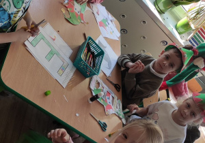 dzieci w czapkach elfów pracują przy stoliku, na nim leżą kolorowanki z literą E