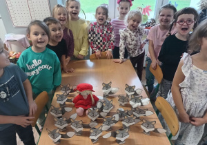 grupa dzieci w klasie, mająotwarte buzie, jakby udawały ryk wilka, na stoliczku leżą wykonane z kartonu wilki i lalka Czerwony Kapturek