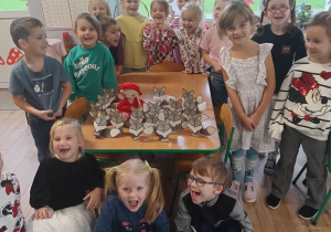 grupa dzieci w klasie, mająotwarte buzie, jakby udawały ryk wilka, na stoliczku leżą wykonane z kartonu wilki i lalka Czerwony Kapturek