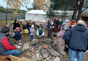 grupa dzieci z rodzicami, zebrani wokół rozpalonego ogniska