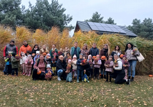 grupa dzieci z rodzicami oraz nauczycielki pozujądo wspólnego zdjęcia na tle ozdobnych miskantów