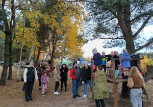 grupa dzieci i rodziców na terenowym placu zabaw, obok stoi nauczycielka