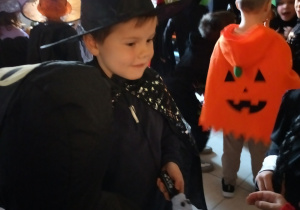 Chłopiec tańczy w trakcie balu. Na sobie ma strój czarodzieja. W tle bawią się pozostałe dzieci.