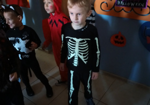 Chłopiec tańczy podczas balu, na sobie ma strój kościotrupa. W tle bawią się pozostałe dzieci.